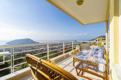 Alanya mulkidagi rattan mebellari bilan jihozlangan balkon, yorqin quyosh nurida ajoyib shahar va dengiz manzaralariga ega.