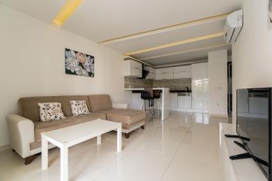 Alanya korteri elutuba koos moodsa valge köögi, beeži diivani ja heledate plaatpõrandatega, mis loovad puhta ja õhulise atmosfääri.