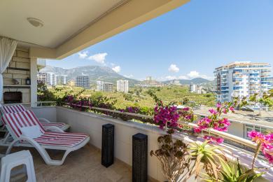 Balkon nekretnine u Alanji sa ležaljkama, svetlim cvećem i zadivljujućim pogledom na planine koji stvara opuštajuću atmosferu.