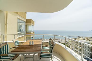 Alanya-Balkon mit Holztisch, gestreiften Stühlen und atemberaubendem Meerblick in einer hellen, luftigen Atmosphäre.