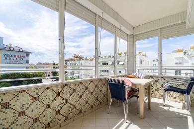 Bright Alanya balcony with tiled walls, a table, chairs, and expansive views through large windows.