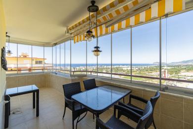 Balkon nekretnine u Alanji sa staklenim zidovima, nameštajem od pruća i zadivljujućim pogledom na more pod jakim, prirodnim svetlom.