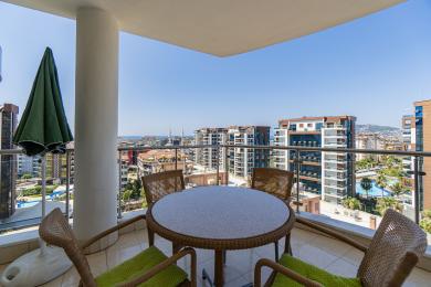 Alanya'daki balkonlu daire, hasır mobilyaları, parlak, güneşli şehir manzaraları ve rahat bir atmosfer sunmaktadır.