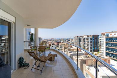 Balkon w Alanyi z meblami z wikliny, wyłożony płytkami, z panoramicznym widokiem na miasto i morze.