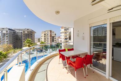 Solrik Alanya-balkong med utsikt over bassenget, med et spisested og en lys og luftig atmosfære.