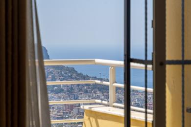 Alanya-Immobilienbalkon mit atemberaubendem Meer- und Stadtblick durch helle, sonnendurchflutete Glastüren und weiße Geländer.