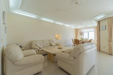 Lichte Alanya woonkamer met crèmekleurige leren banken, tegelvloeren en elegante plafondverlichtingsarmaturen.
