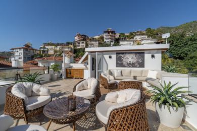 Alanya property featuring a sunny rooftop terrace with wicker furniture, built-in seating, and panoramic views, creating a relaxed atmosphere.
