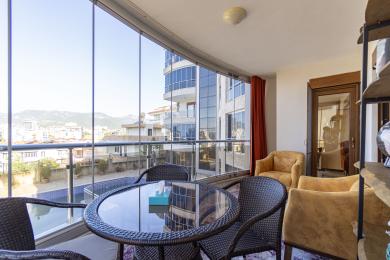 Нерухомість в Аланії: Закритий балкон зі скляними стінами, плетеними меблями та яскравою, повітряною атмосферою з видом на місто.