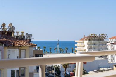 Alanya woning met balkon uitzicht op de Middellandse Zee, palmbomen en helderblauwe luchten.