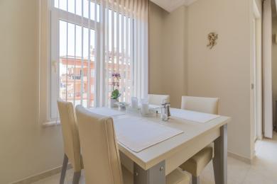 Der helle Essbereich in Alanya verfügt über einen weißen Tisch, cremefarbene Stühle und natürliches Licht durch ein großes Fenster.