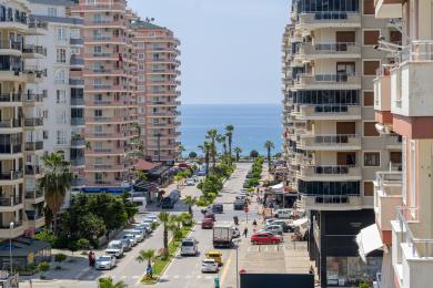 Výhled na nemovitost v Alanyi s ulicí vedoucí k moři, obklopenou moderními bytovými domy a palmami.