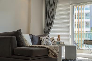 Alanya ejendom stue med en komfortabel mørk sofa, lyst vindue og moderne neutral indretning.
