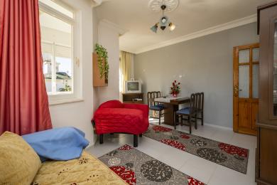 Alanya lejlighed stue med lyst vindue, røde detaljer, flisegulv og hyggelig, beboet atmosfære.
