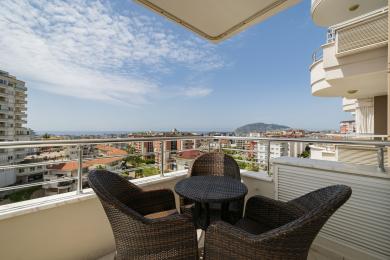 Balkon nekretnine u Alanji sa nameštajem od pruća i zadivljujućim pogledom na grad i more pod vedrim nebom.
