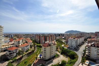 Alanya ejendomsvisning: Et lyst, solrigt bybillede med Middelhavet og bjergene i det fjerne.