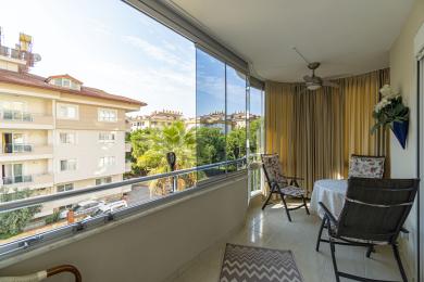 Alanya-Immobilienbalkon mit Glaswänden, Fliesenboden, Sitzgelegenheiten und heller, luftiger Atmosphäre mit Blick auf die Stadt.