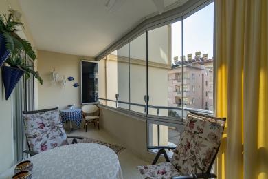 Alanya-Immobilienbalkon mit Glasgehäuse, Blumensitzgelegenheiten und heller, luftiger Atmosphäre mit Blick auf die Stadt.