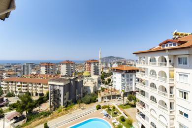 Alanya property balcony view showcasing the city, sea, and pool under bright, sunny skies.