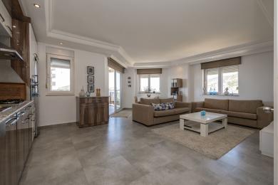 Alanya ejendom: Lyst, åbent opholdsrum med klinkegulve, komfortable sofaer og adgang til balkon, hvilket skaber en afslappet atmosfære.