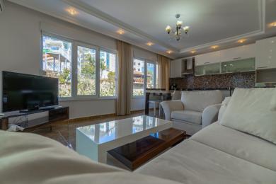 Beyaz kanepeler, modern mutfak, büyük pencereler ve sıcak, davetkar bir atmosfere sahip aydınlık Alanya oturma odası.