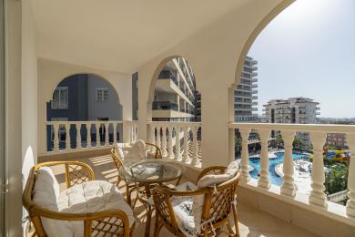 Alanya property balcony with rattan furniture, marble floors, and bright sunlight overlooking a pool.