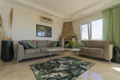 Alanya qonaq otağı neytral divanlar, daş şömine, tropik xalça və parlaq təbii işıqla rahat bir atmosfer yaradır.