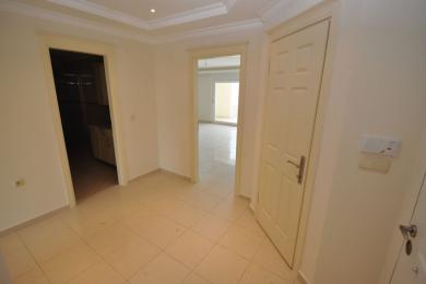 Heller Flur in einem Apartment in Alanya mit Fliesenboden, weißen Wänden und Türen, die zu Küche und Wohnbereichen führen.