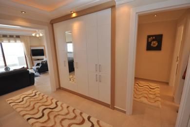 Alanya-Immobilienflur mit einem großen weißen Kleiderschrank mit Holzverkleidung und warmer, einladender Beleuchtung.