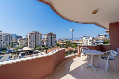 Sunčani balkon u Alanji sa belim stolom i stolicama, koji nudi pogled na grad.