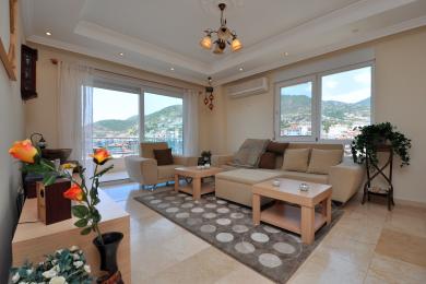 Lys Alanya stue med beige sofaer, marmorgulv og fjellutsikt synlig gjennom store vinduer.