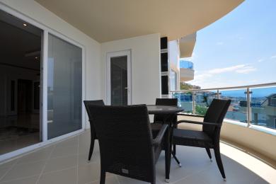 Alanya property balcony with wicker furniture, glass railings, and bright, sunny views of the cityscape.