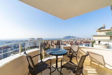 Alanya property balcony with wicker chairs, glass table, and panoramic city and sea views.