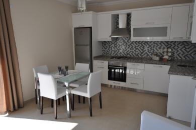 Alanya eiendom kjøkken med hvite skap, mosaikk backsplash, rustfrie stål apparater og et glassbord.
