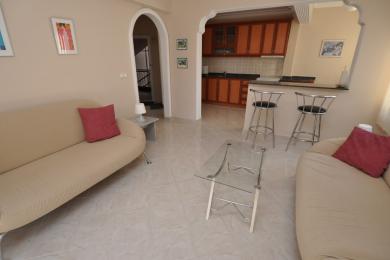 Svetla dnevna soba apartmana u Alanji sa podovima od pločica, sofama i otvorenom kuhinjom sa šankom za doručak.