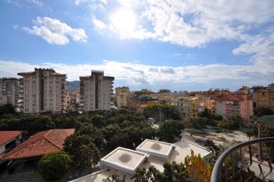 Alanya ejendom med balkonudsigt, der viser bybygninger, frodigt grønt og en lys, solrig og åben atmosfære.