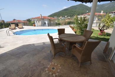 Alanya eiendom terrasse med kurvmøbler, steingulv og et basseng med utsikt over vakre fjell.